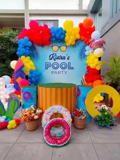 The main backdrop for the pool party, complete with a personalized sign, themed props like flip-flops and lifebuoys, and a vibrant balloon frame.