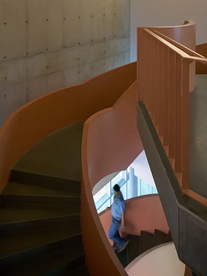 A sculptural spiral staircase at the JSW Vijayanagar complex, with its warm, earthy tones contrasting against the raw concrete walls. This feature is a key element of vertical circulation, designed as both a functional and an artistic statement.