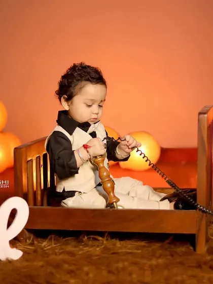 For this first birthday photoshoot, we used a vintage-style theme. The baby boy is sitting in a miniature wooden bed, curiously playing with an old-fashioned telephone prop, creating a charming and unique portrait.
