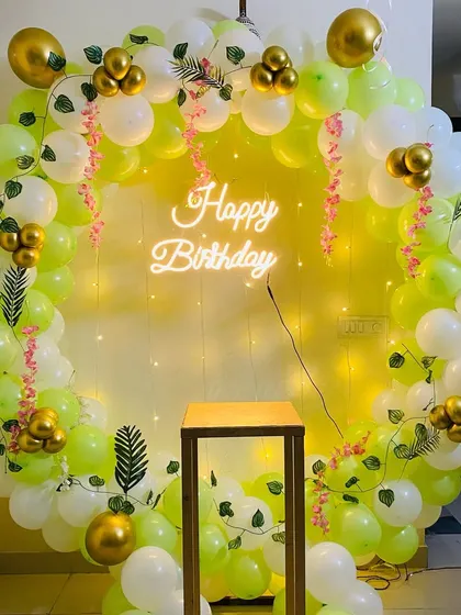 A fresh and natural-looking birthday balloon ring in lime green and white, decorated with artificial vines and a neon sign.