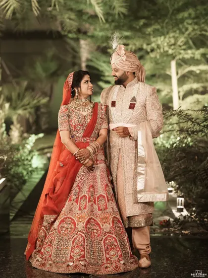 A timeless portrait of the bride and groom against a lush, green backdrop. Her red lehenga and his elegant sherwani create a stunning contrast.