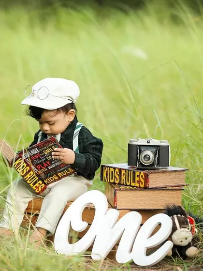 An outdoor first birthday shoot for a little gentleman. The natural setting and vintage props like the old camera and books create a timeless, storybook feel.