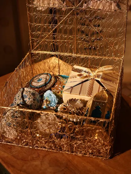 A golden wire mesh box filled with blue and gold themed items, including evil-eye coasters and a decorative lantern.