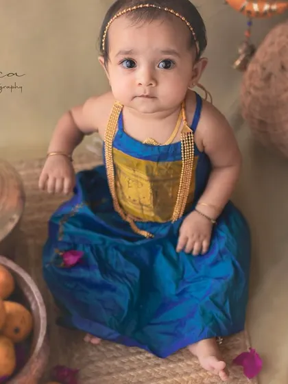 A beautiful portrait of a baby girl amidst baskets of mangoes. The composition and styling create a rich, textured image that feels like a classic Indian painting.
