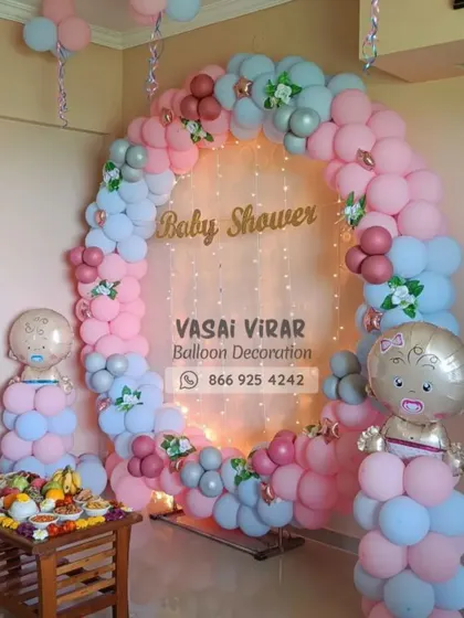 This baby shower decoration uses a softer, pastel color palette. The ring backdrop is decorated with pink, blue, and grey balloons, with small floral details and fairy lights in the center for an elegant and modern look.