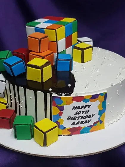 A puzzlingly fun cake for a 10th birthday. This Rubik's Cube cake features a half-and-half design with a chocolate drip and dozens of colorful, edible cubes tumbling down the side.