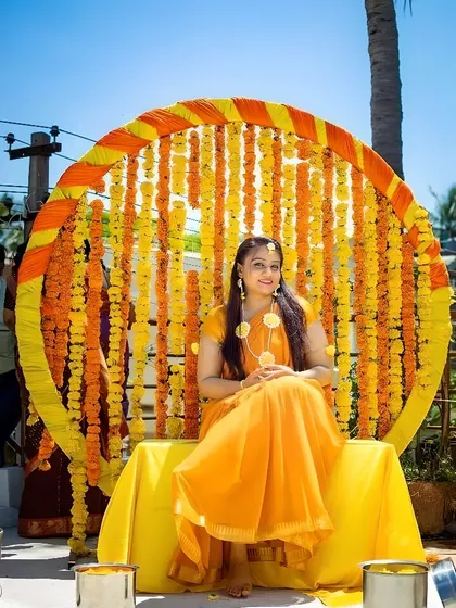 For traditional functions like a Haldi ceremony, I design vibrant backdrops like this one. It features a large circular frame decorated with strings of real marigold flowers, creating the perfect setting for photos.