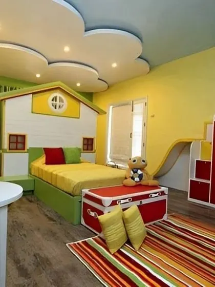 This vibrant kids' room is all about fun. It features a house-shaped bed, a slide, and a playful cloud-themed false ceiling, turning the bedroom into an indoor playground.