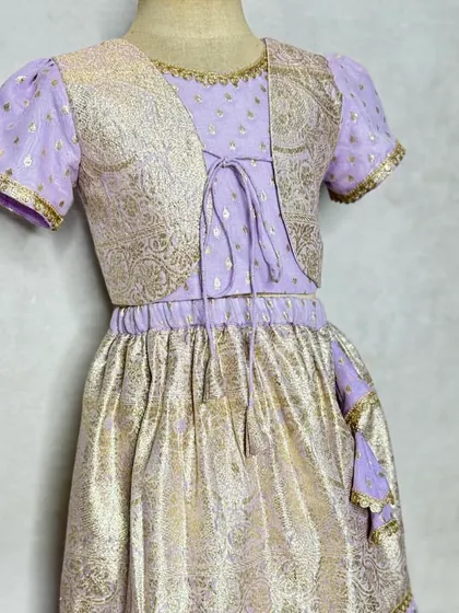 This lavender and gold lehenga set includes a short, embroidered jacket for a layered look. The metallic brocade fabric gives it a festive shimmer.