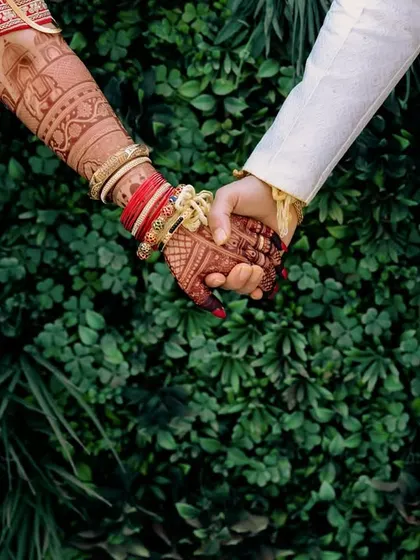 A close-up of the couple's hands, showcasing the bride's intricate henna and traditional red bangles. This detail shot symbolizes the joining of two lives in a Marathi wedding.
