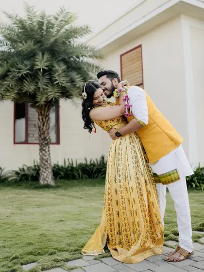 A sweet and playful moment from a Haldi shoot. The groom gives the bride a loving kiss on the cheek as they embrace in a garden setting.