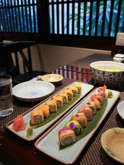 A beautiful table set with our signature rolls. In the foreground, the Rainbow Roll shows off its colors, while the Super California Roll sits ready to be enjoyed, showcasing the variety we offer.