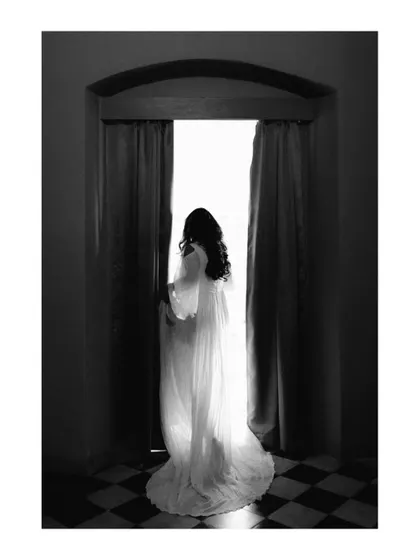 A stunning silhouette of a bride standing in a doorway, bathed in bright light. This artistic black and white shot is dramatic and full of emotion, symbolizing her step into a new life.