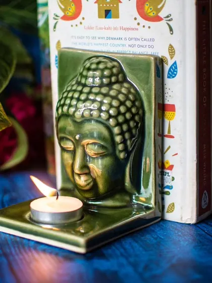 Another look at the Buddha tealight holder used as a bookend. The warm candlelight against the books creates a cozy and inviting atmosphere, perfect for a reading nook.