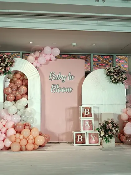 A lovely "Baby in Bloom" theme with a soft pink color palette. The setup includes arched backdrops, floral accents, and "BABY" blocks for a classic baby shower look.