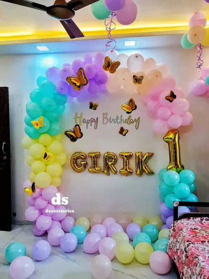 A beautiful butterfly-themed first birthday decoration. The pastel rainbow balloon arch is adorned with delicate golden butterflies, creating an enchanting and gentle theme for a little one.