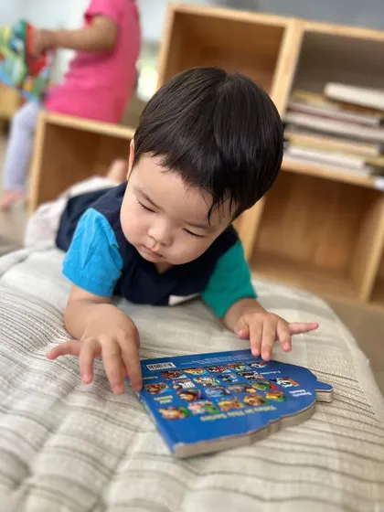 A young boy lies on a cushion, deeply engrossed in a picture book. We create comfortable spaces that invite children to read.