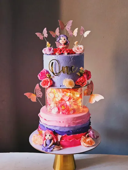 This stunning multi-tiered cake for a first birthday features a beautiful light-up separator, cascading butterflies, and fresh flowers. The design combines different textures and elements to create a truly magical and eye-catching centerpiece.