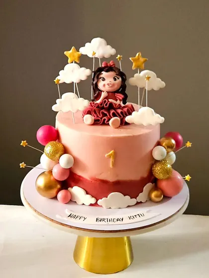 A first birthday cake for a little princess, featuring a handcrafted figurine in a beautiful red dress, surrounded by edible clouds and stars.