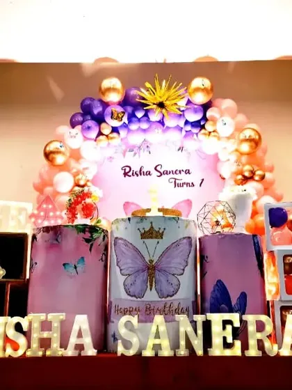 A vibrant butterfly theme for Risha Sanera's first birthday. The decor uses bold colors and large butterfly cutouts to create a lively and eye-catching display.