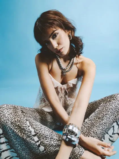 A seated portrait with a direct, engaging gaze. The bright blue background contrasts with the wild prints, making the image pop.