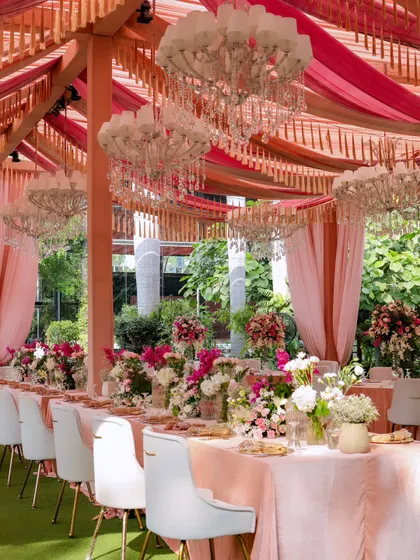 An elegant outdoor luncheon with long tables set under a canopy of pink drapery and white chandeliers. The setup is perfect for a sophisticated daytime celebration.