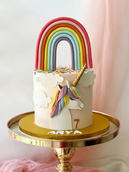 This unicorn cake features a large, impressive rainbow arching over the top. The side of the cake has a unicorn profile, and the top is covered in colourful sprinkles.