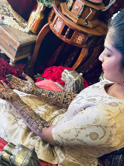 A candid shot of a bride admiring her full bridal mehendi. The design extends up her arms, filled with traditional motifs that complement her elegant attire.