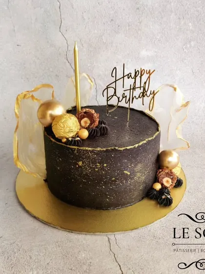 This isn't a chocolate cake. It's a 1 kg Mango Luxe cake with a black buttercream finish, gold splatters, and rice paper sails, showing that any flavor can be dressed up for an elegant event.