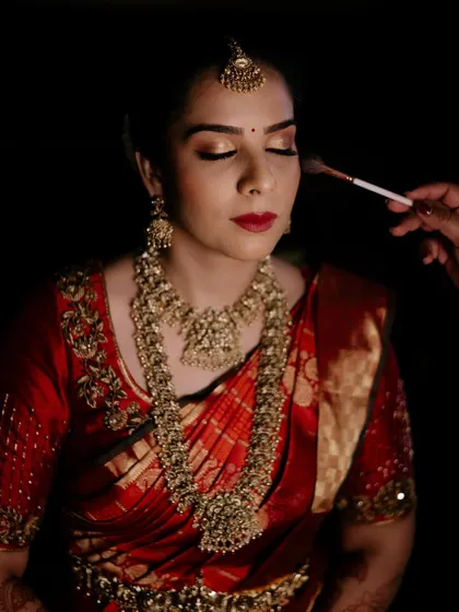 Bride Parinitha getting her makeup done. This shot captures the artistry involved in creating a flawless base and shimmering gold eyes for her big day.