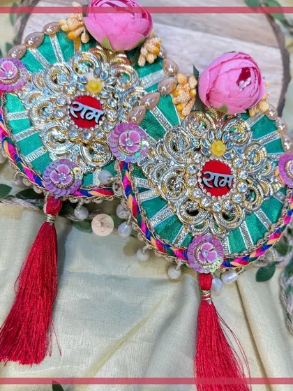A beautiful green "Ram Ram" hanging with pink floral details and red tassels, perfect for adding a touch of nature-inspired elegance.