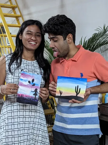 A couple having fun and being silly while showing off their watercolor paintings.