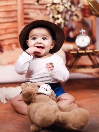 A candid moment of a baby boy playing with his teddy bear during a rustic-themed studio session.
