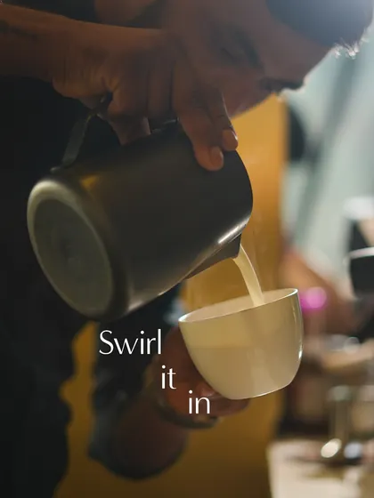 The art of the pour. My barista carefully swirls the frothed milk into the espresso to create intricate latte art.