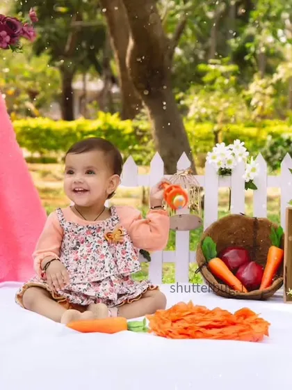 A happy one-year-old enjoying her outdoor picnic, set up with a pretty pink tent and colorful props.