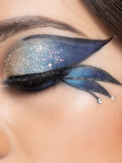 An extreme close-up of a model's eye, showcasing intricate, winged makeup with blue and silver glitter. This image is a testament to my skill in beauty photography, capturing fine details for makeup artists and beauty brands.