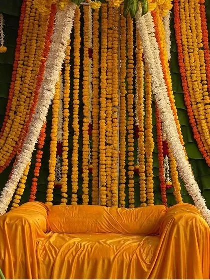 A traditional Haldi seating area with a sofa covered in yellow fabric, set against a backdrop of banana leaves and dense marigold garlands.