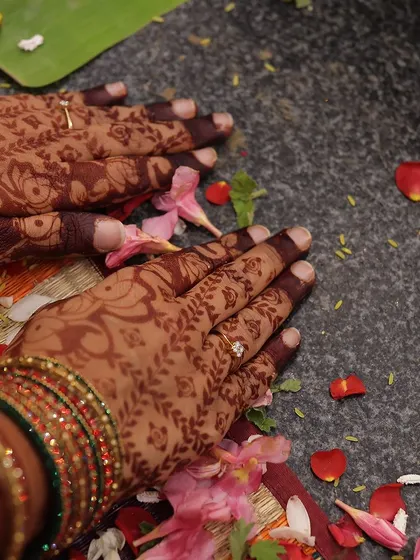 An artistic shot of the bride's hands during a ritual, with flower petals scattered around, highlighting the henna stain.