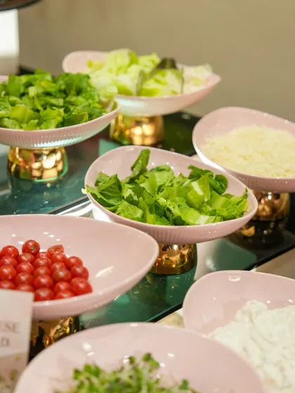 A fresh salad bar with a variety of greens, vegetables, and cheeses in elegant pink bowls. We provide healthy, customizable options to ensure there is something for everyone.
