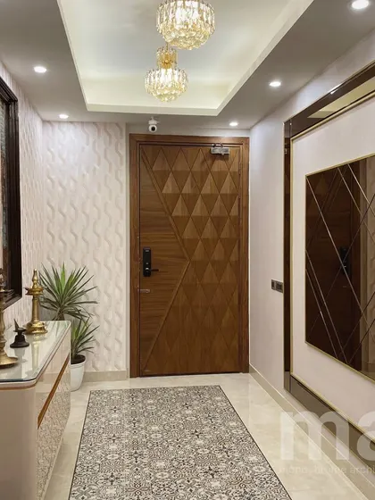 A view of the foyer showing the designer door with a geometric diamond pattern, a 3D textured wallpaper, and a large wall mirror with a metallic frame. These elements come together to create a luxurious and welcoming entryway.
