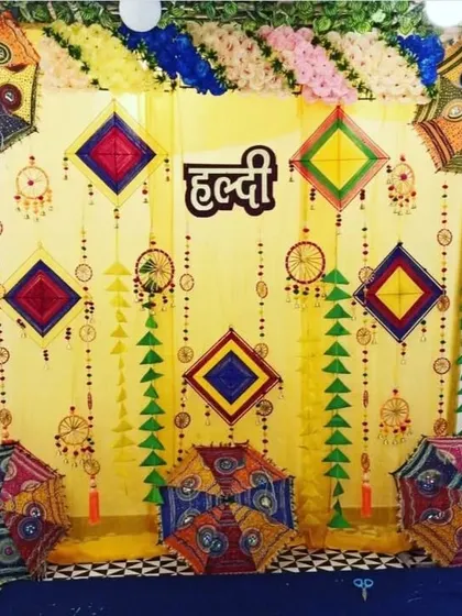 A festive Haldi backdrop featuring a yellow curtain decorated with colorful kites, dreamcatchers, and Rajasthani umbrellas.