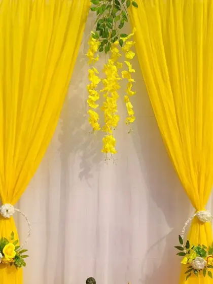 A minimalist yet elegant Ganpati backdrop. The focus here is on the beautiful yellow drapes and the hanging floral arrangement in the center, creating a serene and graceful space to place the idol.
