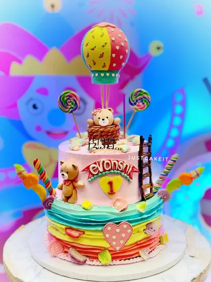 A colorful 5kg Nutella chocolate cake for a first birthday. The design is a fantasy of color, featuring a teddy bear in a hot air balloon and lots of candy accents.
