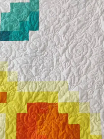 A detail shot of another pixelated rose quilt, this one in a warm sunset palette of yellow, orange, and teal.