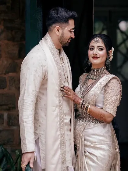 A vision in white. The groom's off-white sherwani with subtle embroidery and a matching stole creates a serene and elegant look, perfectly harmonizing with the bride's silver-white saree.