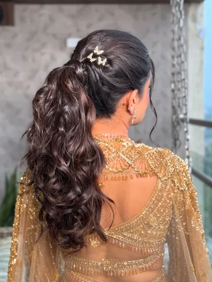 A view of the chic, curly ponytail adorned with butterfly clips. This modern hairstyle adds a playful touch to the glamorous golden look.