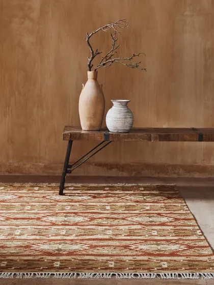 A close-up shot of a patterned rug on the floor, paired with a rustic bench and decor. This in-context view helps customers visualize the rug in a real home setting.