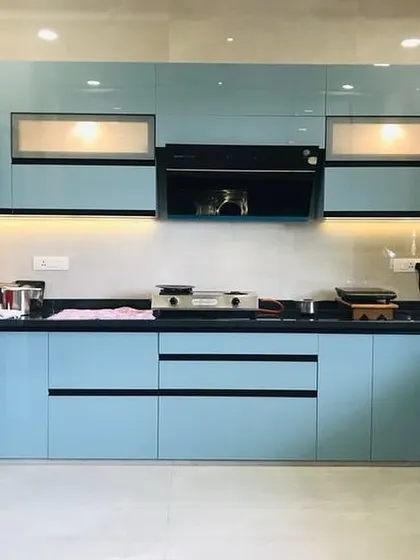 A vibrant and modern kitchen featuring glossy sky-blue cabinets with integrated black profile handles. The under-cabinet lighting and built-in chimney complete the clean and stylish aesthetic.