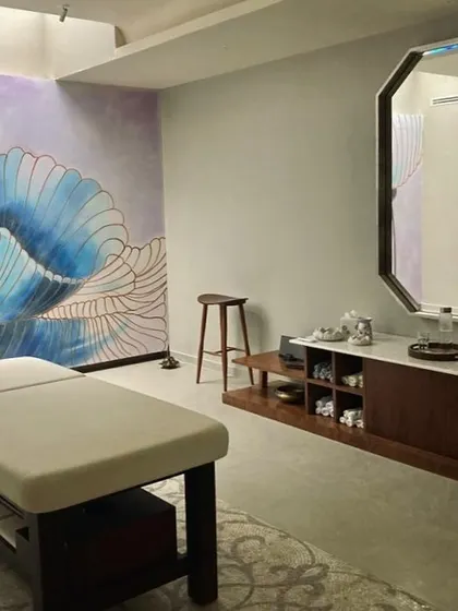 A spa and wellness room designed for ultimate relaxation. A large, hand-painted floral mural in calming blue tones serves as the serene backdrop for the massage table, while the clean lines of the wooden console keep the space uncluttered.