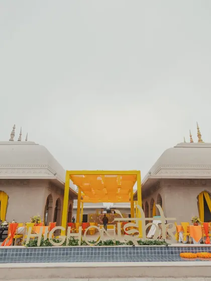A poolside setup for a Haldi ceremony, featuring a large, custom hashtag sign and a yellow canopy structure against the architectural beauty of Fairmont Jaipur.